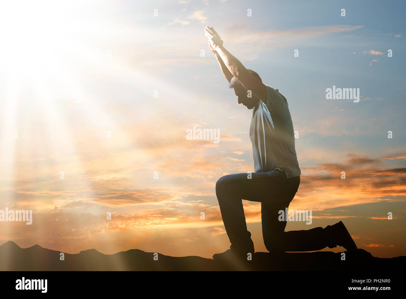 Side View Of A Man Kneeling And Praying Against Cloudy Sky At Sunset