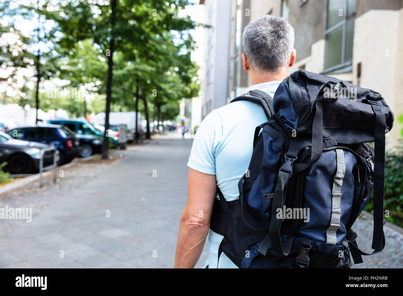 Rear View Of A Man With Backpack Walking On Pavement Stock Photo - Alamy