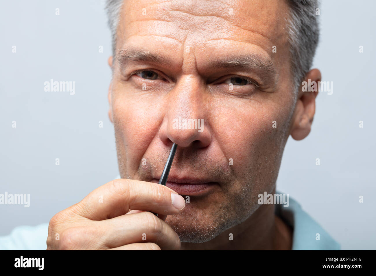 Portrait Of A Mature Man Plucking Nose Hair With Tweezers Stock