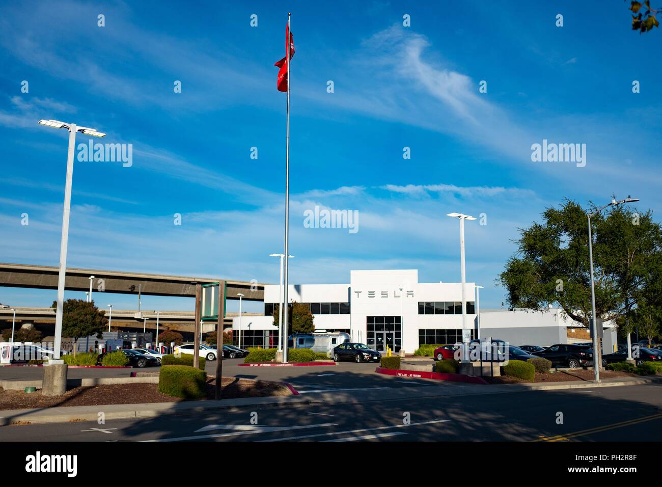 Tesla flag flying outside large Tesla dealership, with multiple parked Tesla Motors automobiles visible, Pleasanton, California, July 23, 2018. () Stock Photo