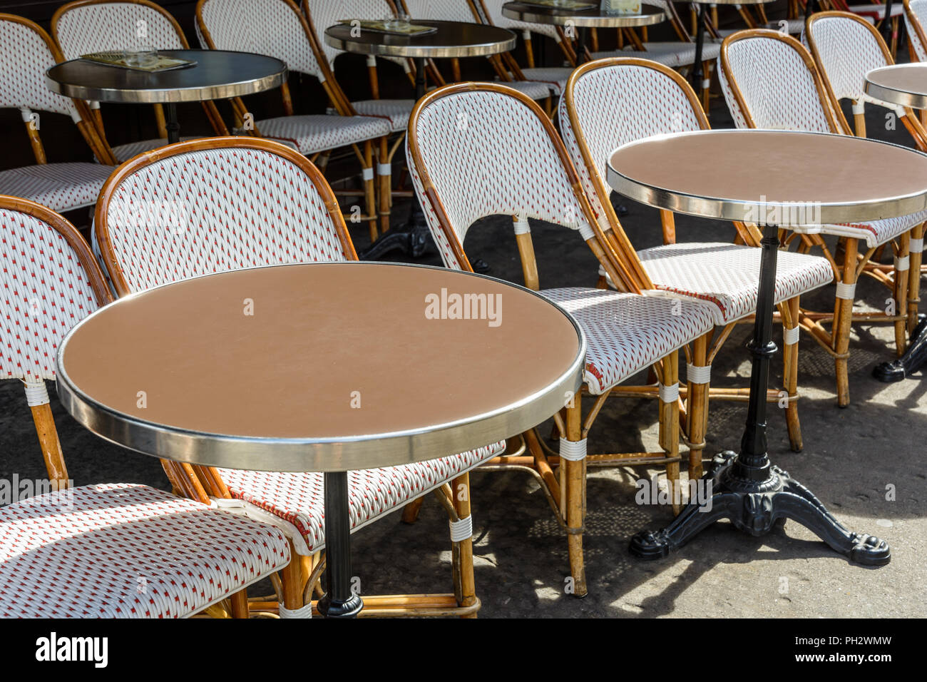 A typical terrace outside of a parisian brasserie set up with rattan chairs and small round tables with a cast iron leg. Stock Photo
