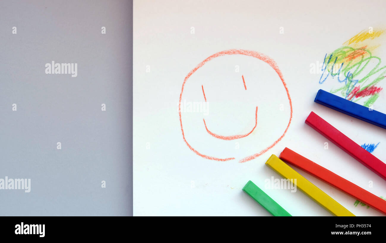 Colorful pastel sticks with a smiley face drawn on a drawing pad, with some empty space on the left Stock Photo