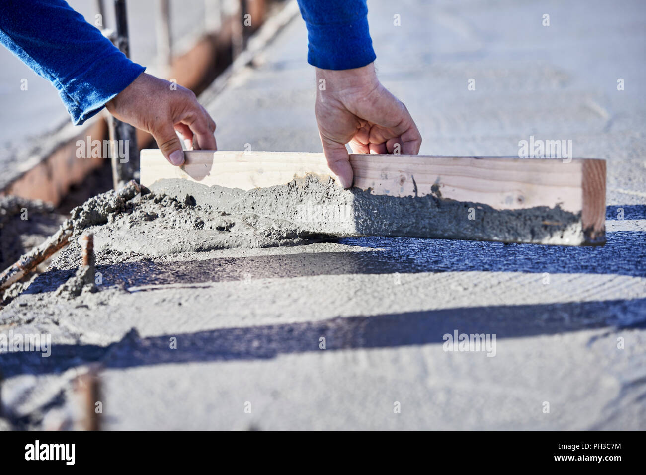 The hands of a mason using a piece of wood to level and move wet cement