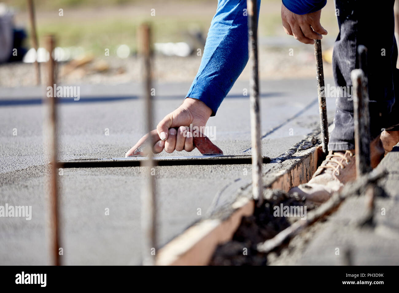 A mason using a concrete trowel to finish a newly poured concrete slab