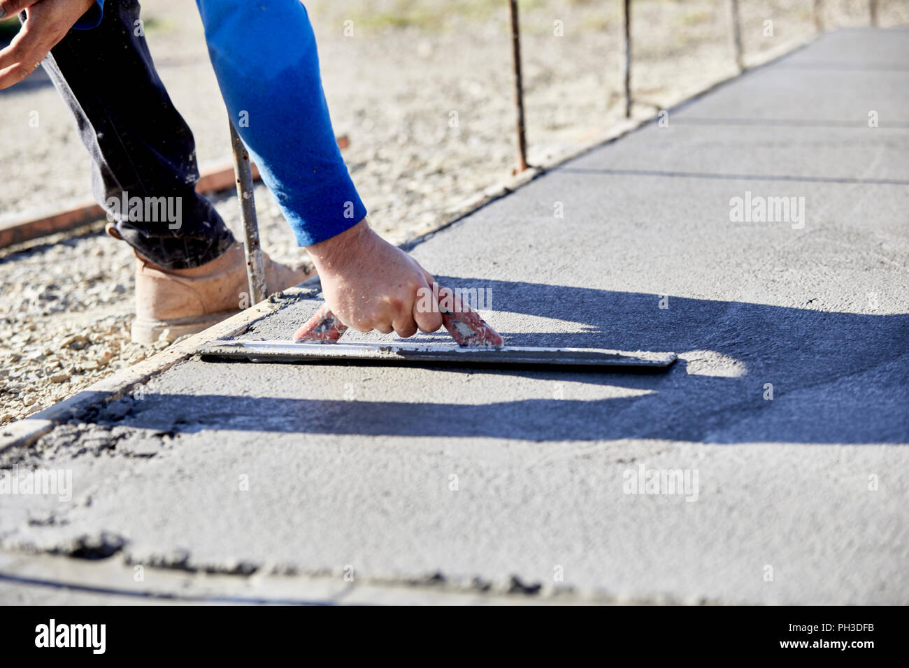 A mason using a concrete trowel to finish a newly poured concrete slab