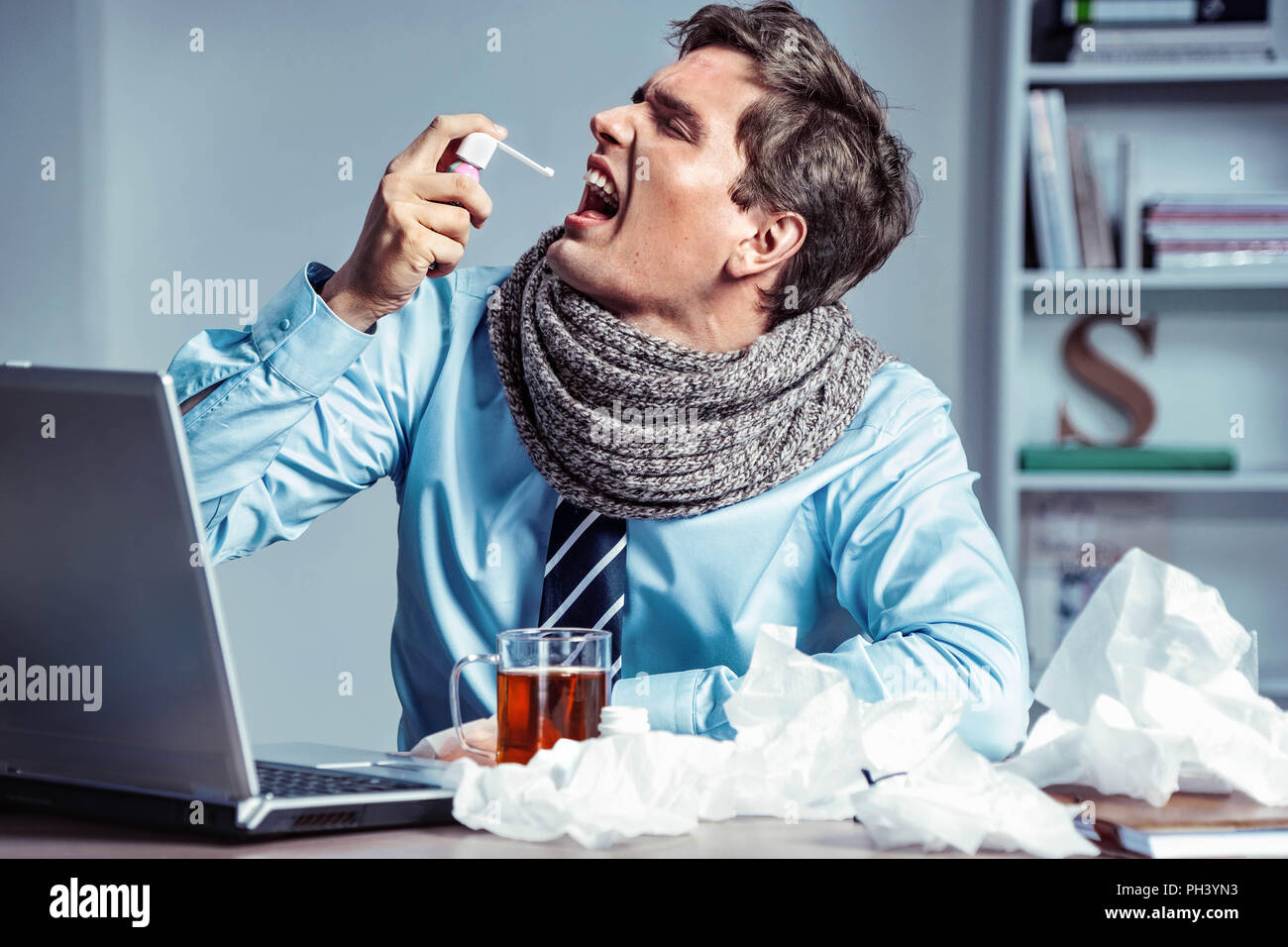 Sick employee using spray for throat. Photo of young man in office suffering virus of flu. Medical concept. Stock Photo