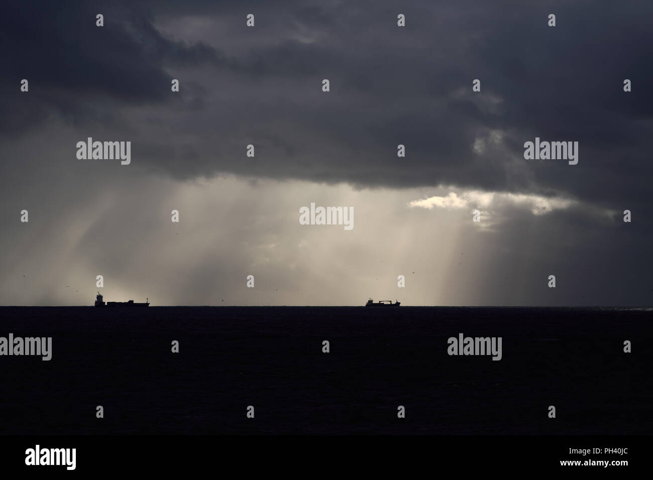 Silhouette of commercial ships in the horizon against dramatic sky with ...