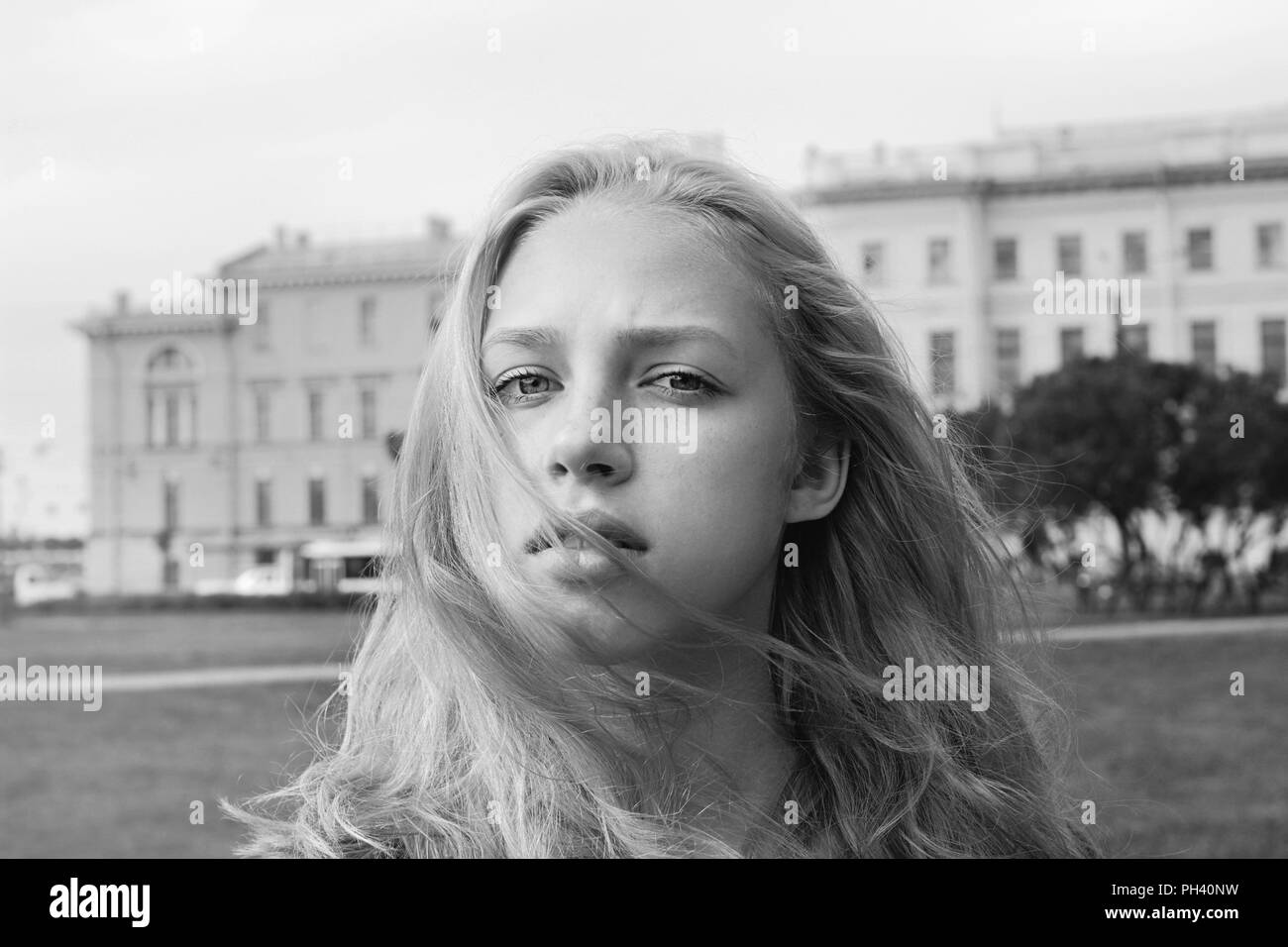 A young girl with blond long hair on a background of a city park. Black and white. Stock Photo