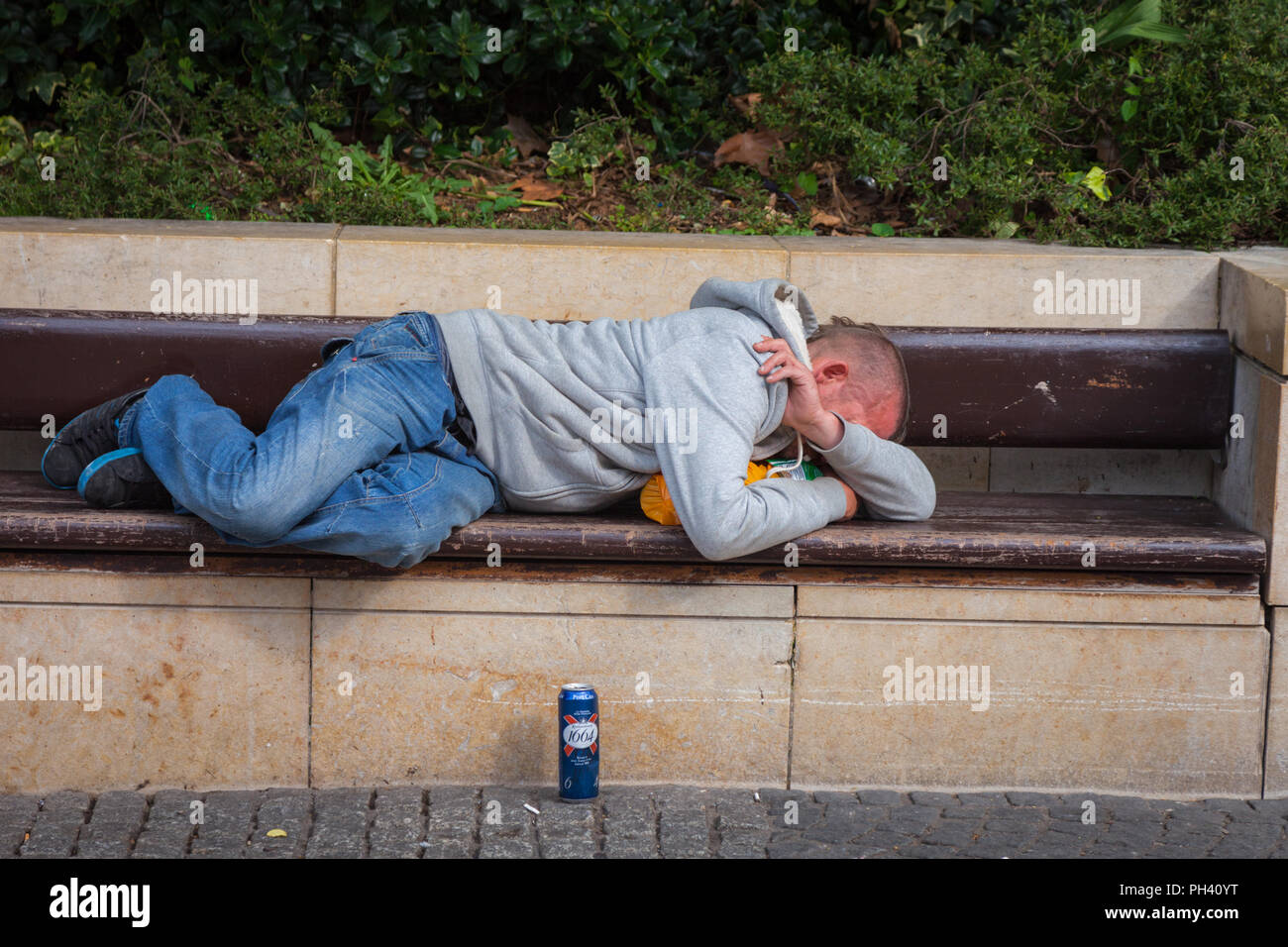 Man lying asleep on a public bench who may be drunk and asleep, Bristol UK Stock Photo