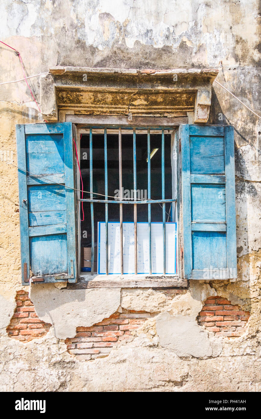 Old window with bars and blue shutters in old building with peeling plaster and exposed brickwork Stock Photo