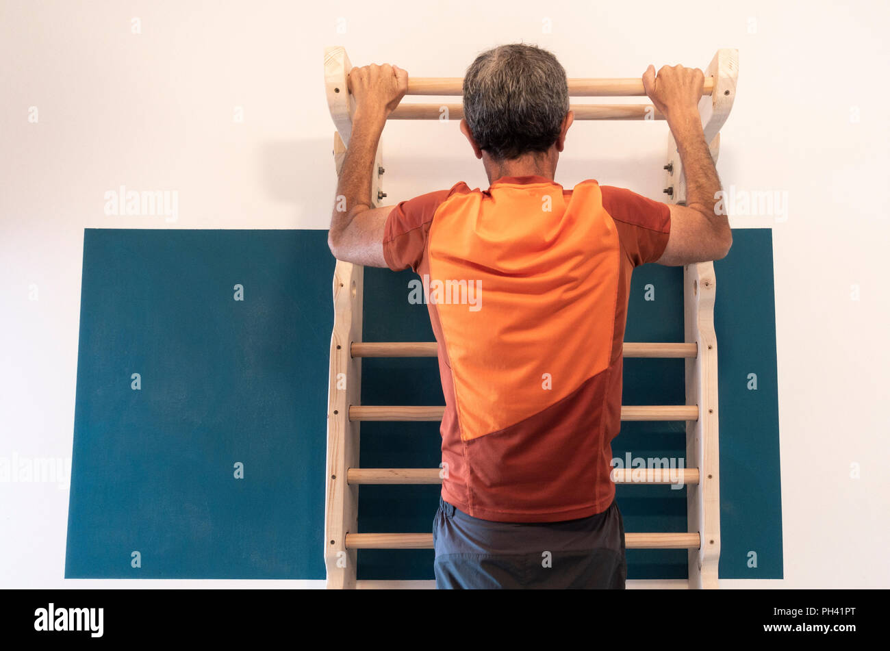 61 year old man exercising at home on homemade wall bars in small apartment. Stock Photo