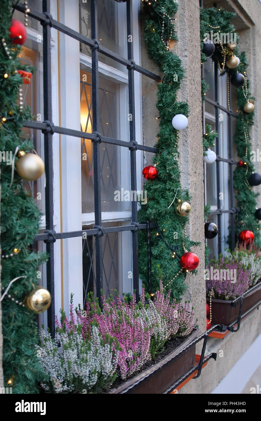 Window, view from outside, decorated with beautiful christmas decorations, lights, baubles, blooming heaathers, green garlands. Stock Photo