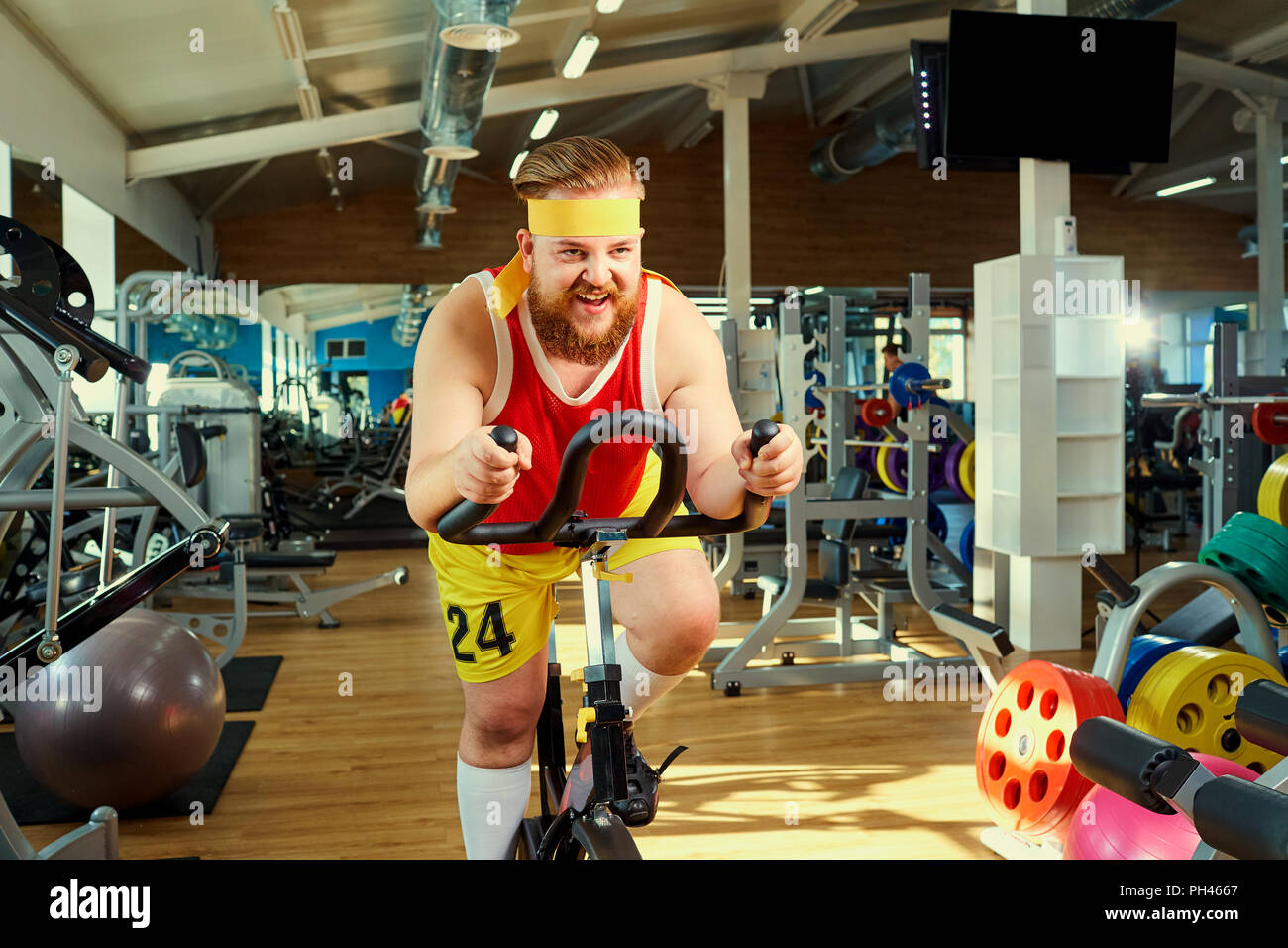 A funny fat man  doing exercises on an exercise bike in a sports Stock Photo