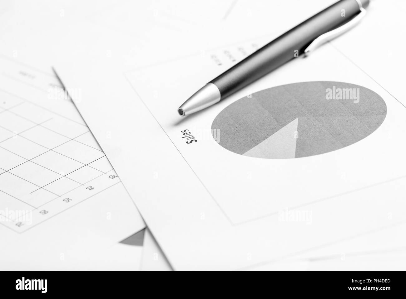 Monochrome image of ballpoint pen lying on a business document with pie graph, focus to the text Sale. Stock Photo