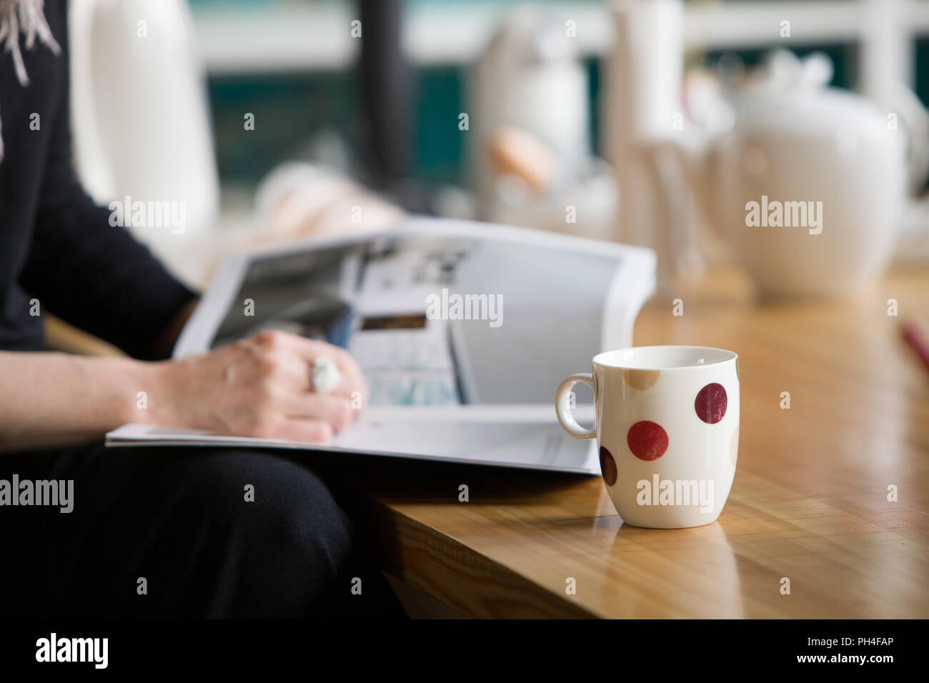 Woman with a big nice ring reading a magazine and drinking tea at a wooden table. Relaxing in a cafe and enjoying tea or coffee. Stock Photo