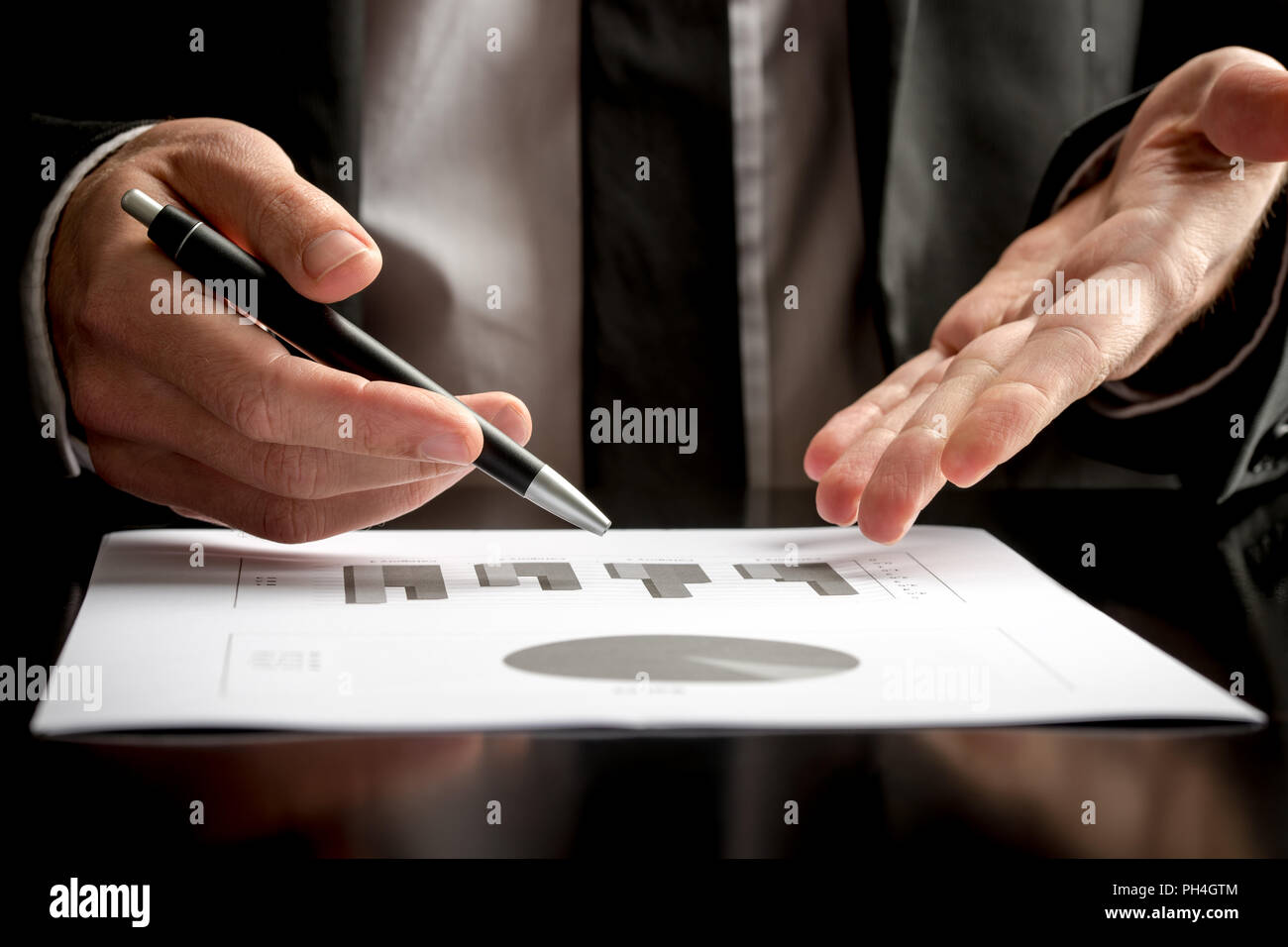 Businessman in a meeting or presentation holding a pen in one hand and pointing with the other to a document on the table in front of him, close up vi Stock Photo