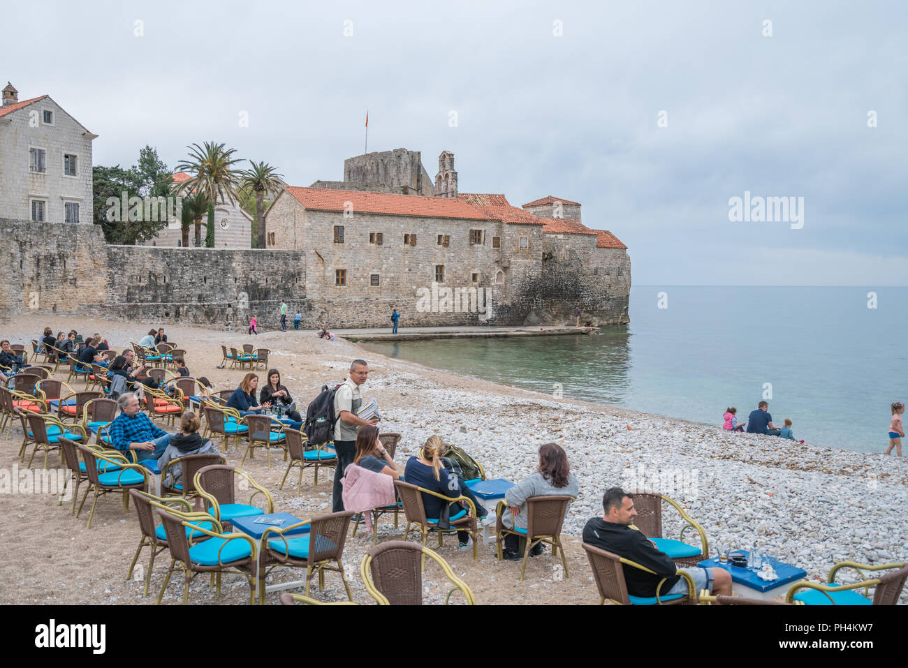Budva, Montenegro - April 2018 : Tourists sitting on  chairs on the beach outside a cafe, enjoying coffee, refreshments and desserts Stock Photo