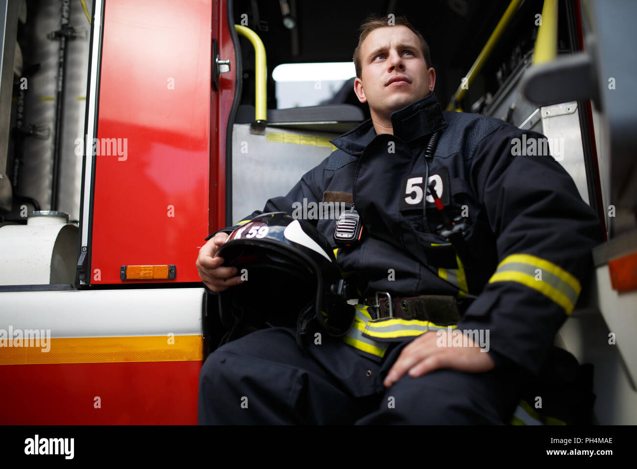 Photo of young fireman with helmet in hands sitting in fire engine ...