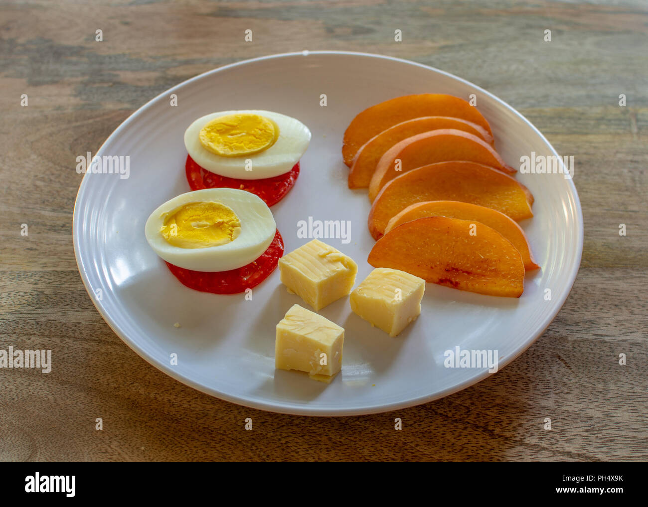 Sliced yellow peach on white plate with a boiled egg, tomatoes and cheese on aged wood background - healthy low-carbohydrate meal rich in proteins Stock Photo