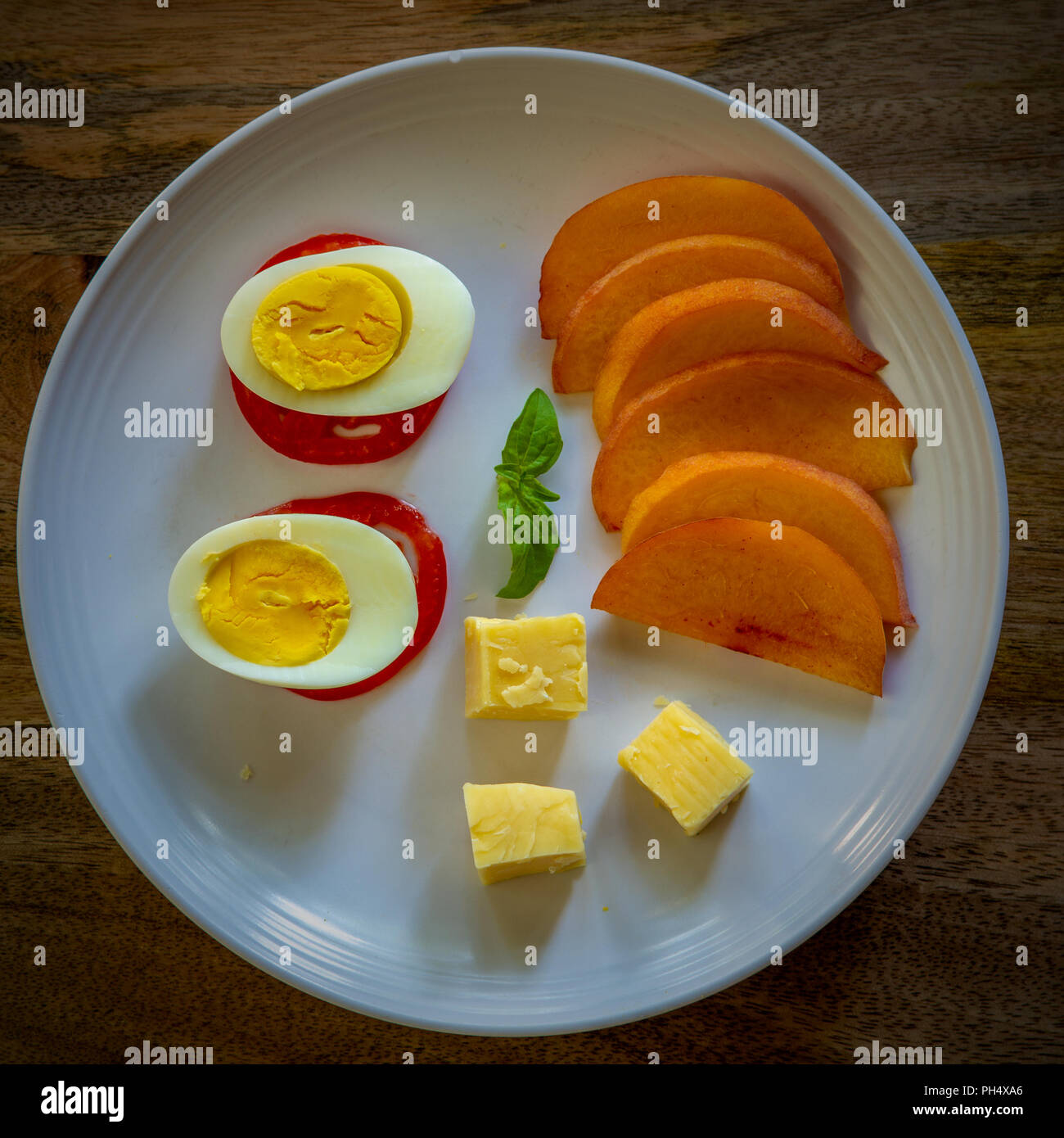Sliced yellow peaches on white plate with a boiled egg, tomatoes and cheese on aged wood background - healthy low-carbohydrate meal rich in proteins Stock Photo