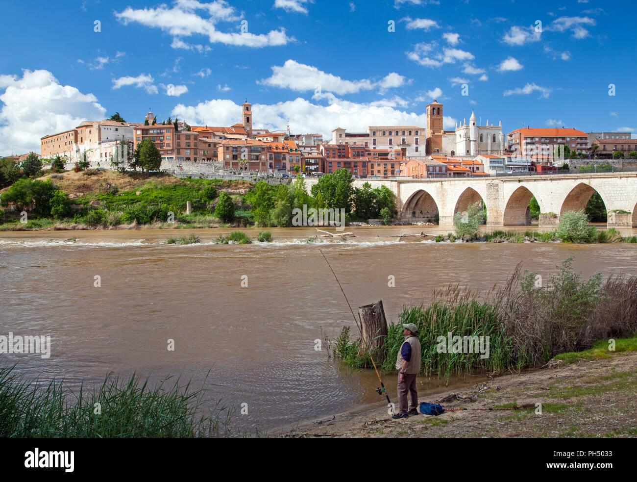 Man fishing from  the man made beach on the river Douro with a view of the medieval town of Tordesillas in the distance Spain Stock Photo