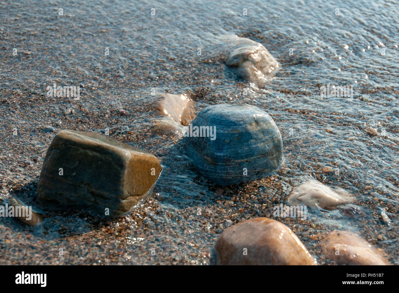A group of pebbles by the sea shore partly immersed in sea water Stock Photo