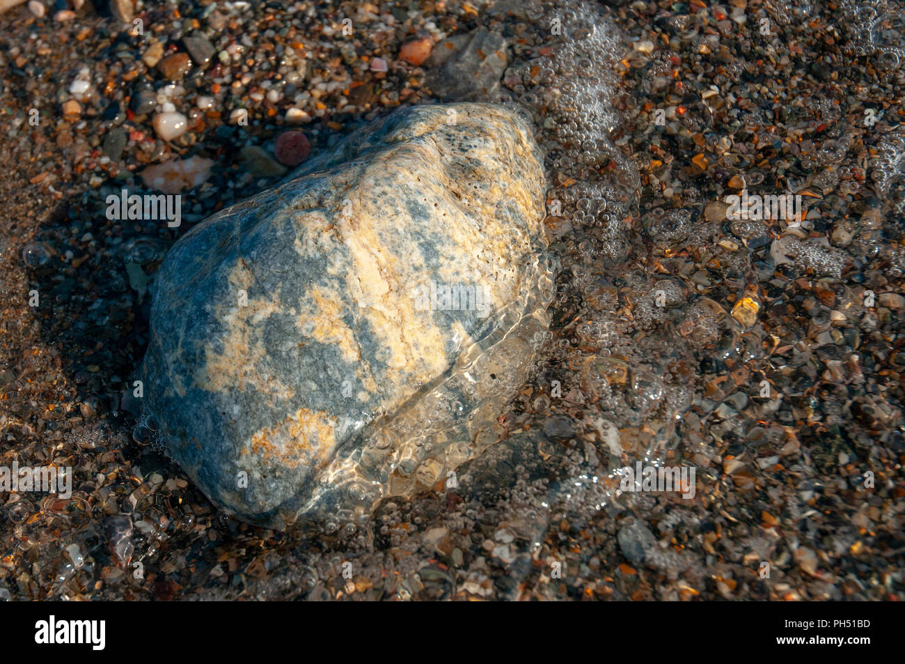 A group of pebbles by the sea shore partly immersed in sea water Stock Photo