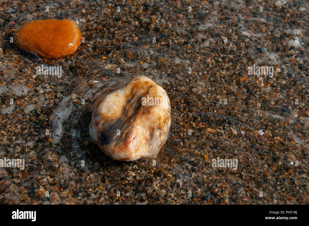 two small wet pebbles near the shoreline partially immersed in the water Stock Photo