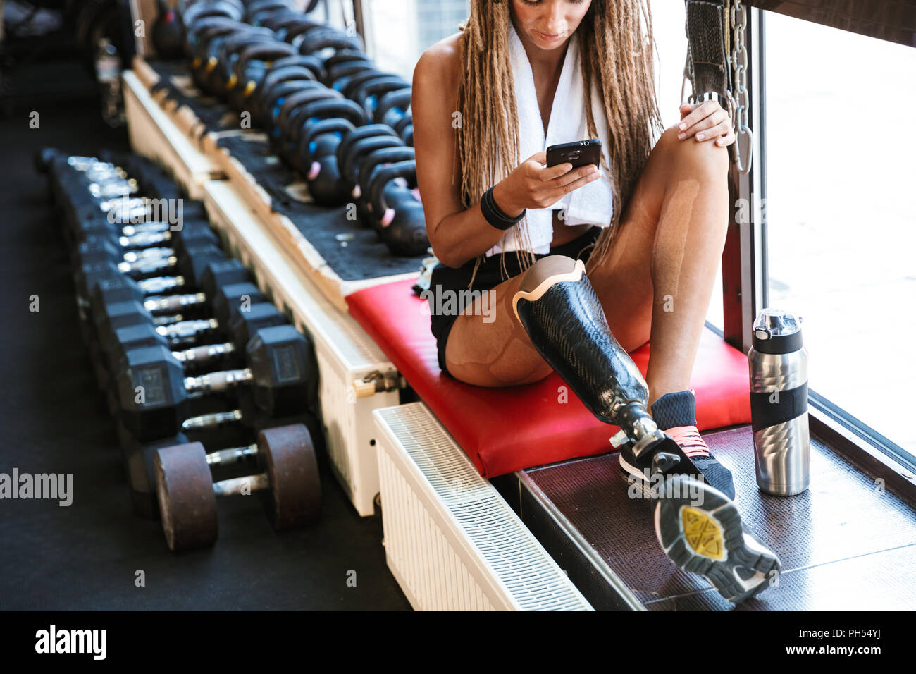 Image of strong disabled sports woman sitting in gym using mobile phone. Stock Photo