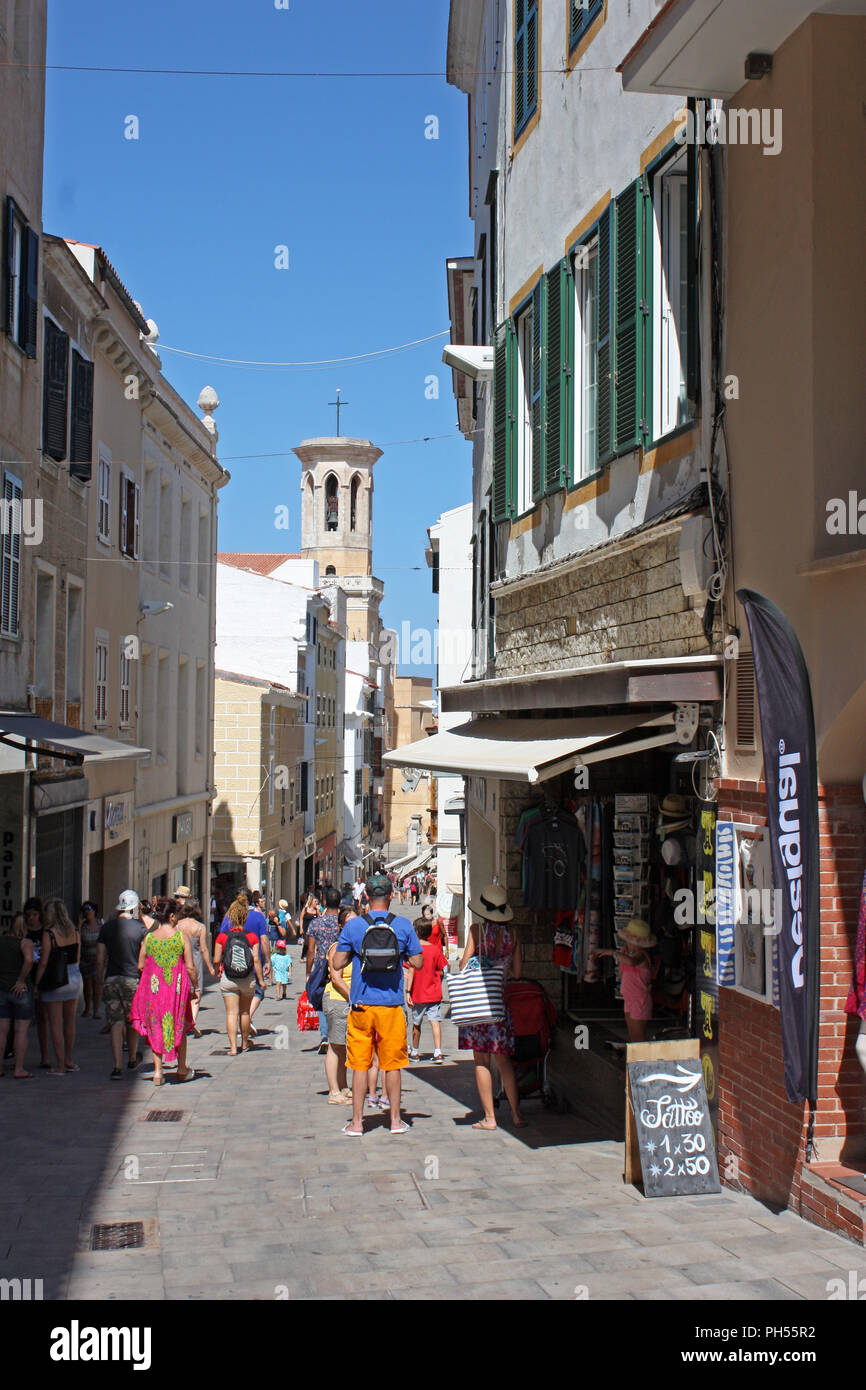 Spain. Balearic Islands, Menorca, Mahon. City centre. Narrow street with pedestrians and cathedral of Santa Maria bell tower in background. Stock Photo