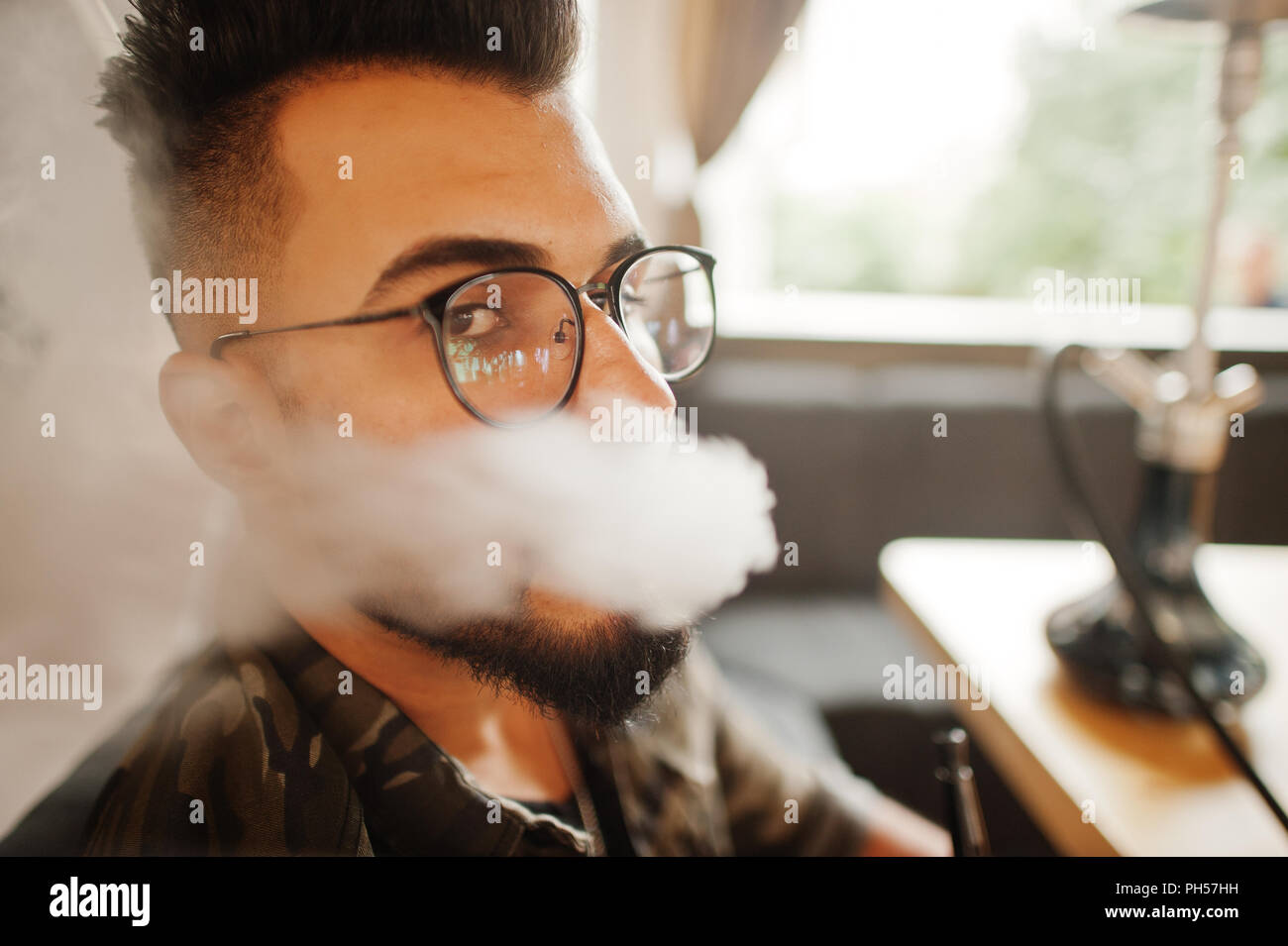 Close up head of stylish beard arabian man in glasses and military jacket  with smoke smoking hookah at street bar. Arab model having rest Stock Photo  - Alamy
