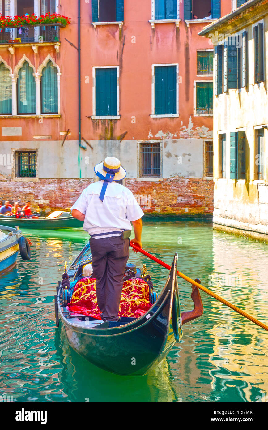 Gondolier drives tourists in his gondola on canal in Venice Stock Photo