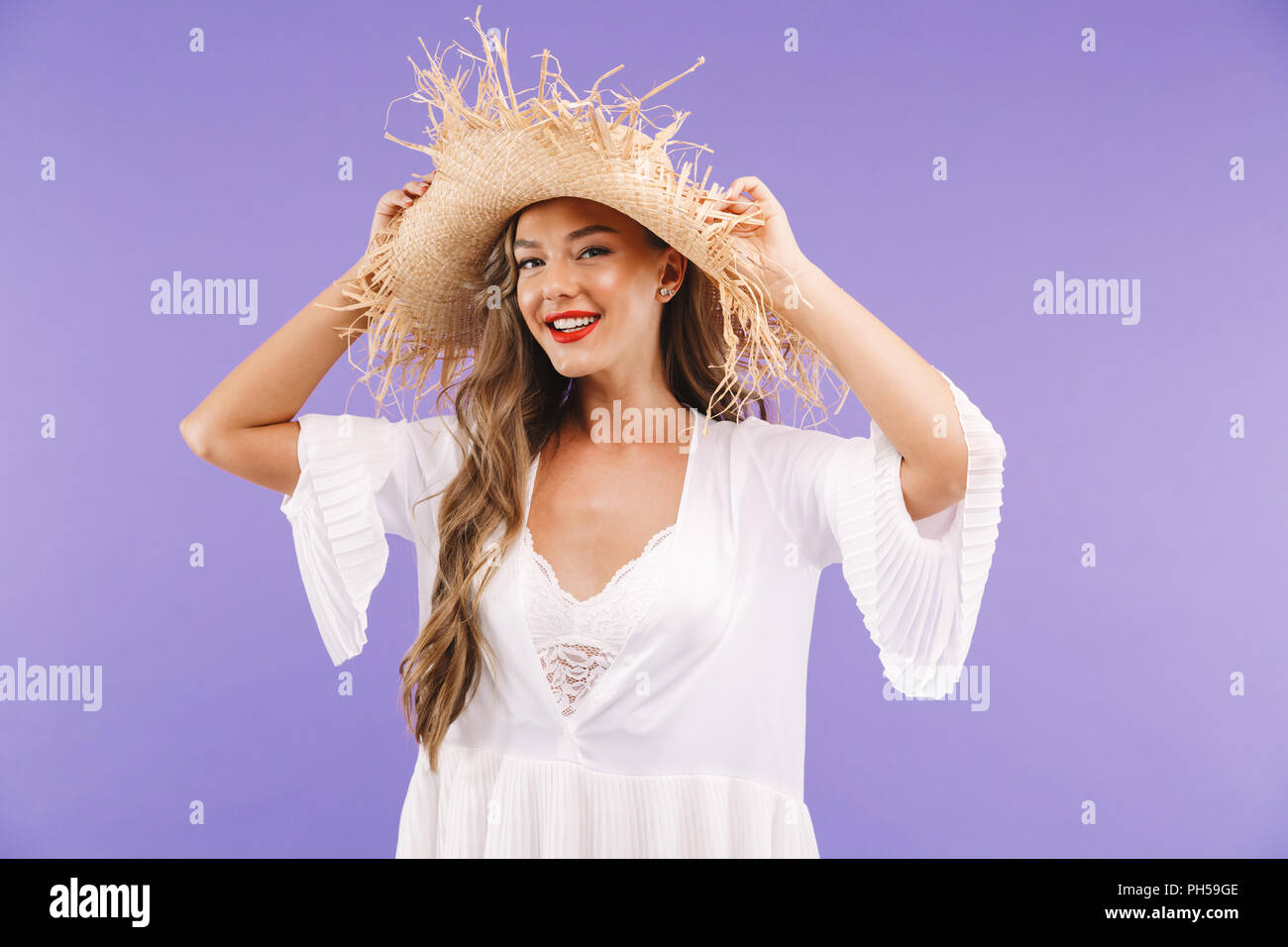 Portrait of a smiling young woman in white dress and straw hat posing ...