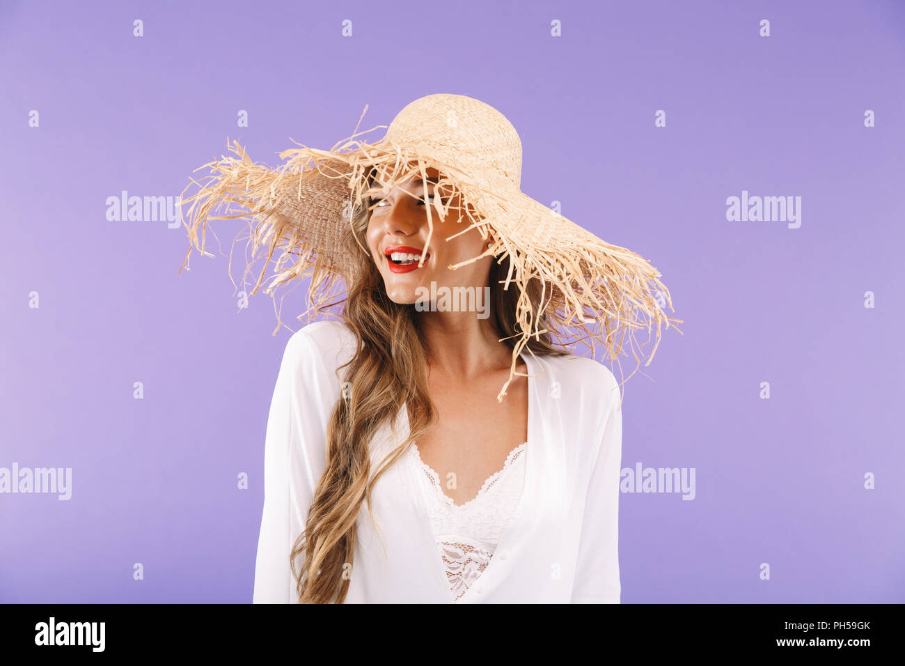 Portrait of a happy young woman in white dress and straw hat posing ...