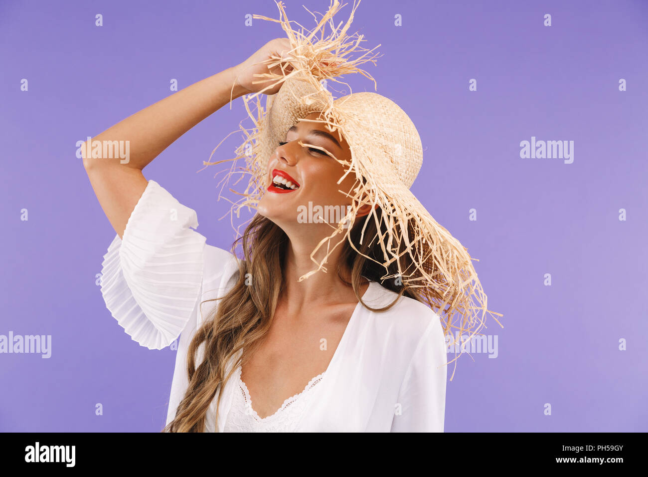 Portrait of a laughing young woman in white dress and straw hat posing ...