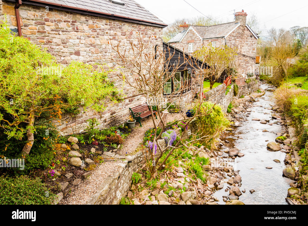 A bench by a stream and housing in a small Welsh village Stock Photo