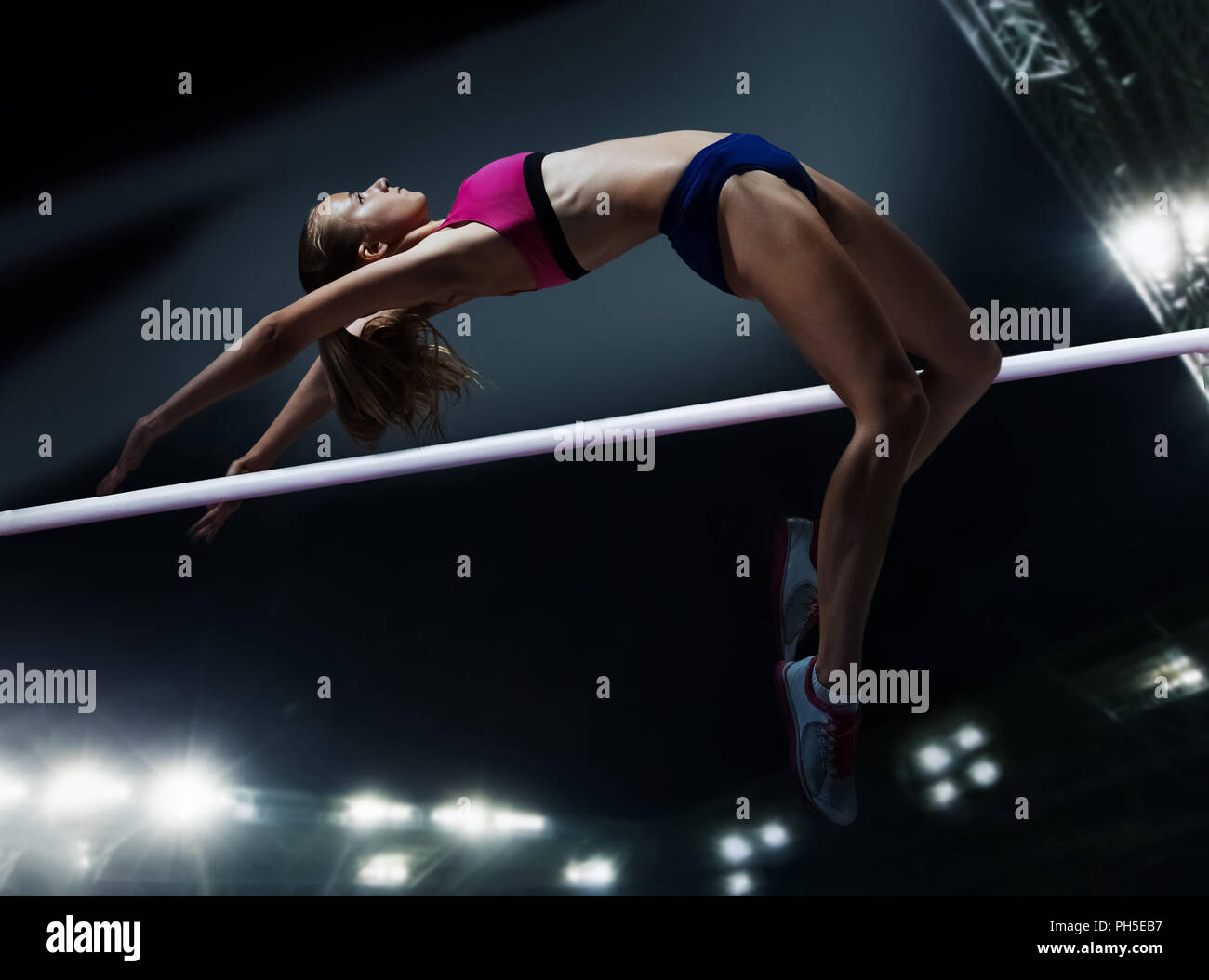 The female athlete in action. high jump over bar at stadium at night