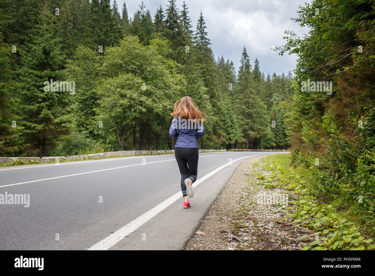 Running girl on the road. Young slim woman jogging in mountains. Rear ...