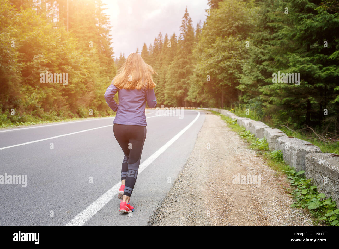 Running girl on the road. Young slim woman jogging in mountains. Rear ...
