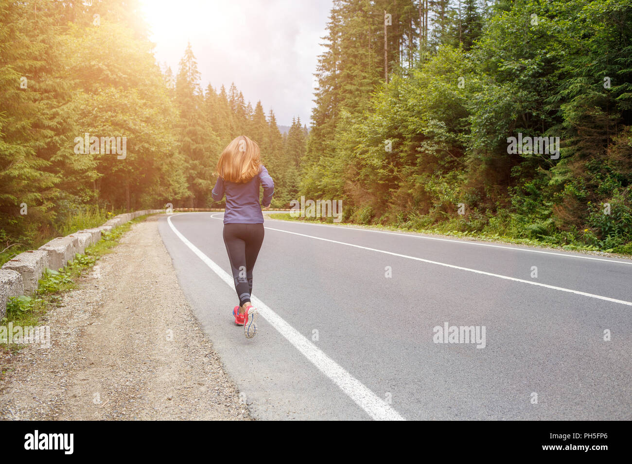 Running girl on the road. Young slim woman jogging in mountains. Rear ...