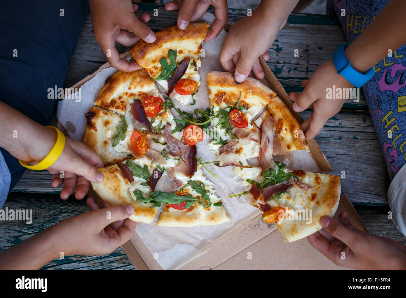 Top view image of children grab slices of pizza from box at the outdoors picnic. Children hands taking pizza Stock Photo