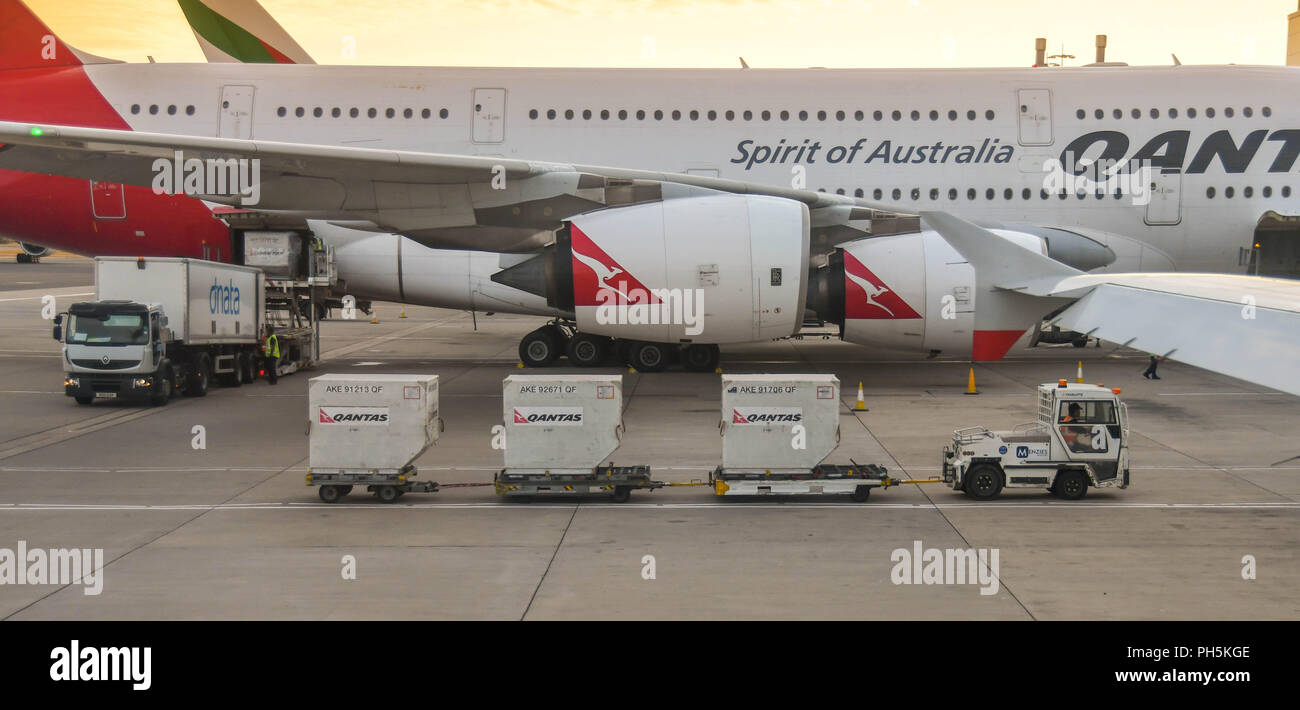 Air freight pallets on trailers being towed past a Qantas Airbus A380 jet at London Heathrow airport. Stock Photo