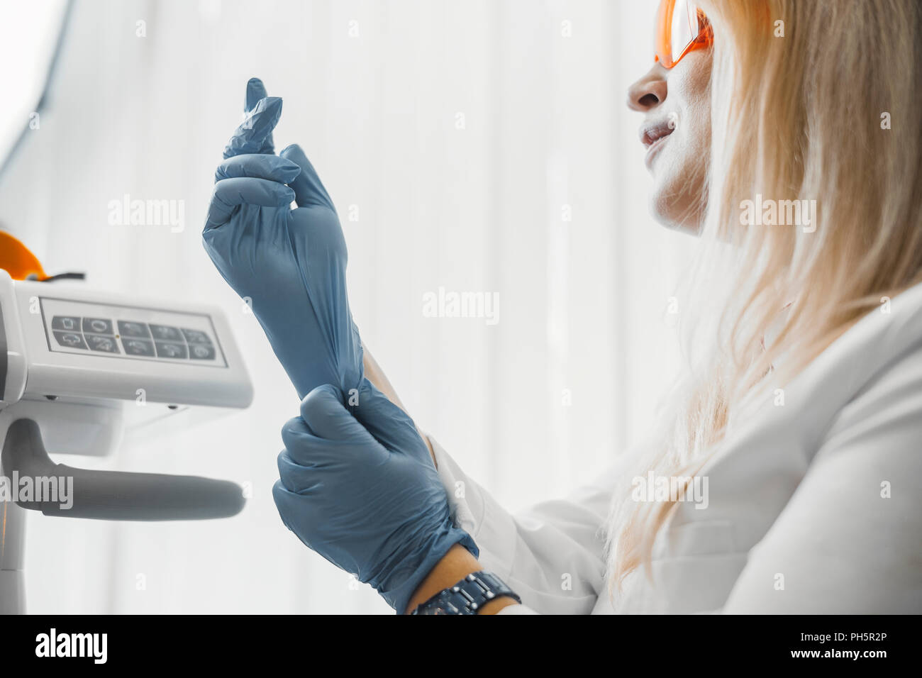 Woman dentist sitting next to dental equipment and putting on gloves