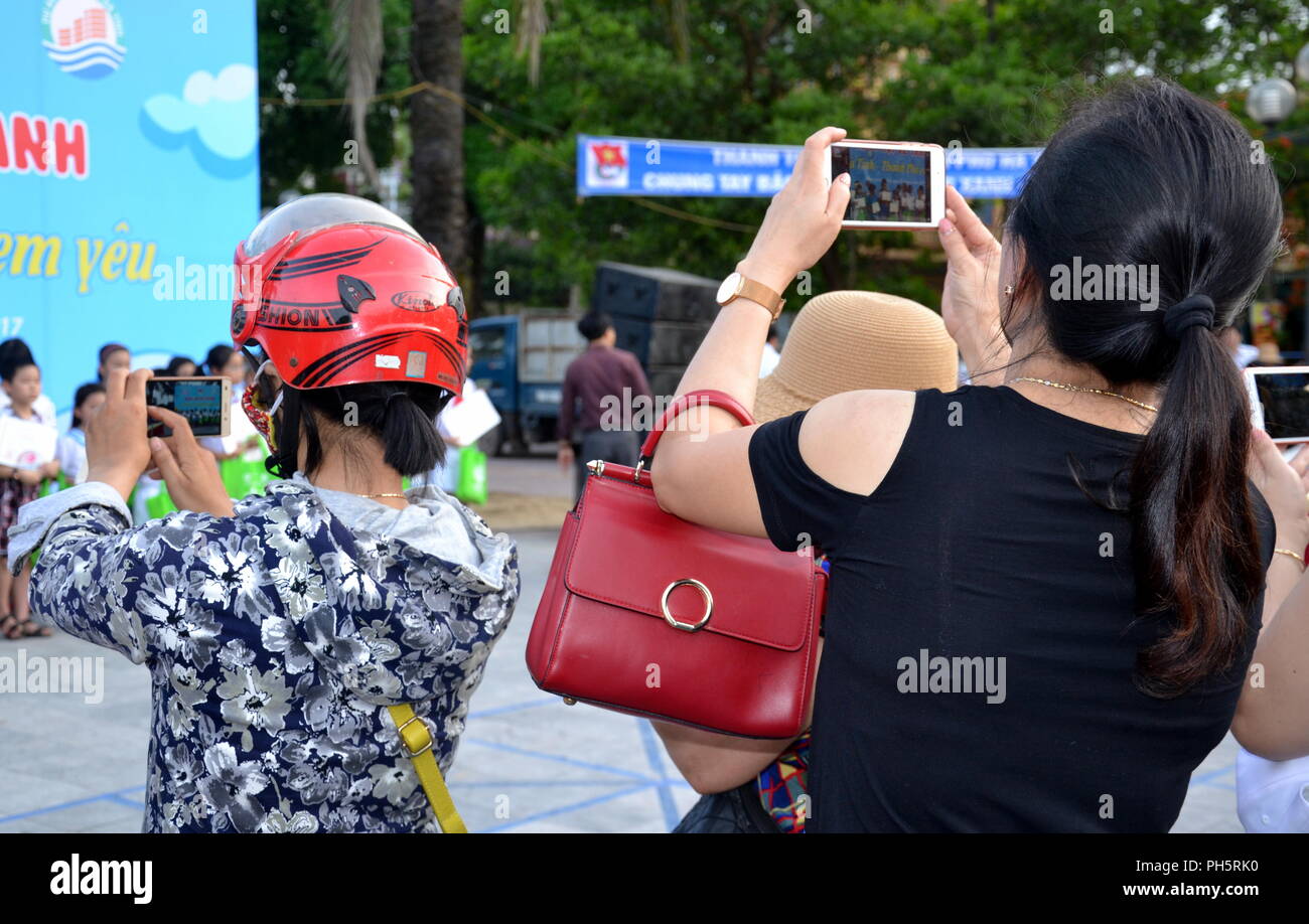 Two Vietnamese women taking photos on their mobile phones Stock Photo