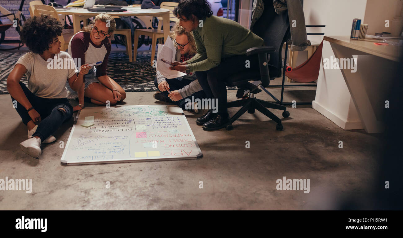 Group of young people discussing over new app development. Four startup colleagues sitting on floor and planning over software and programming for new Stock Photo