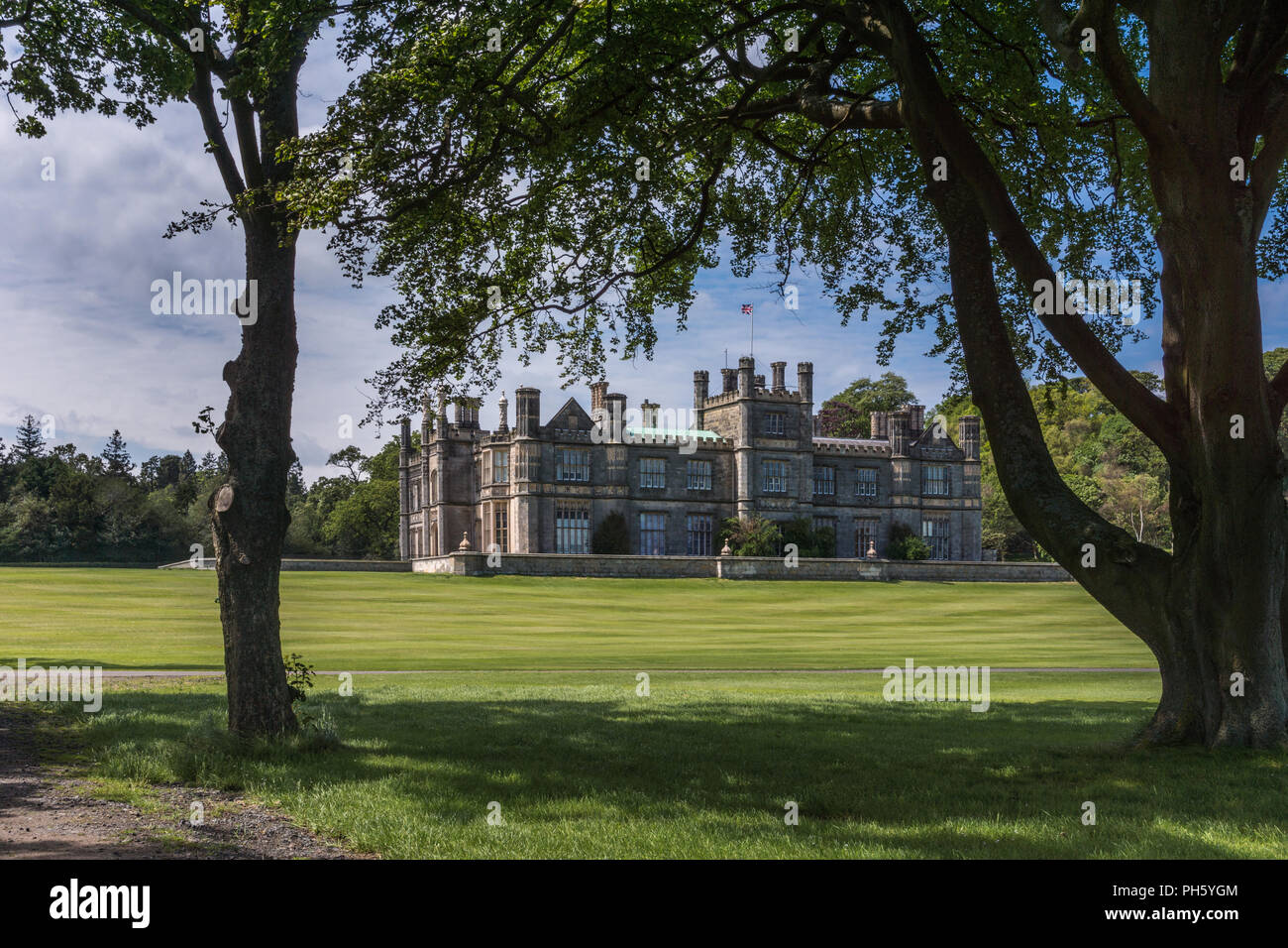 Edinburgh, Scotland, UK - June 14, 2012: Dalmany house, mansion and castle in Tudor revival style as seen from under foliage of woods. Blue sky. Stock Photo