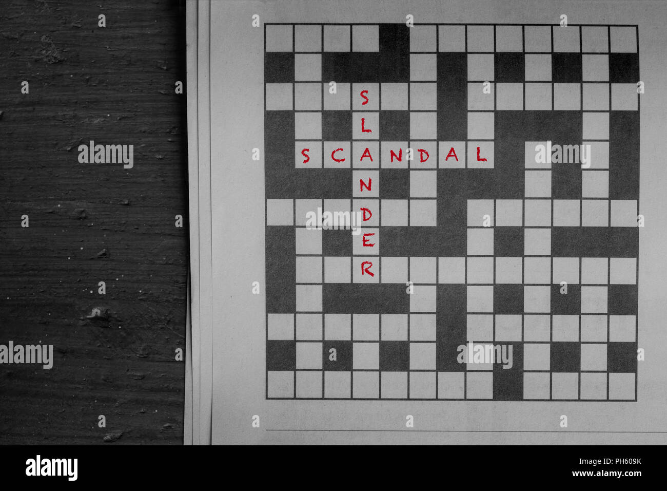 Scandal and slander written in red as solutions to a newspaper crossword puzzle on wood Stock Photo