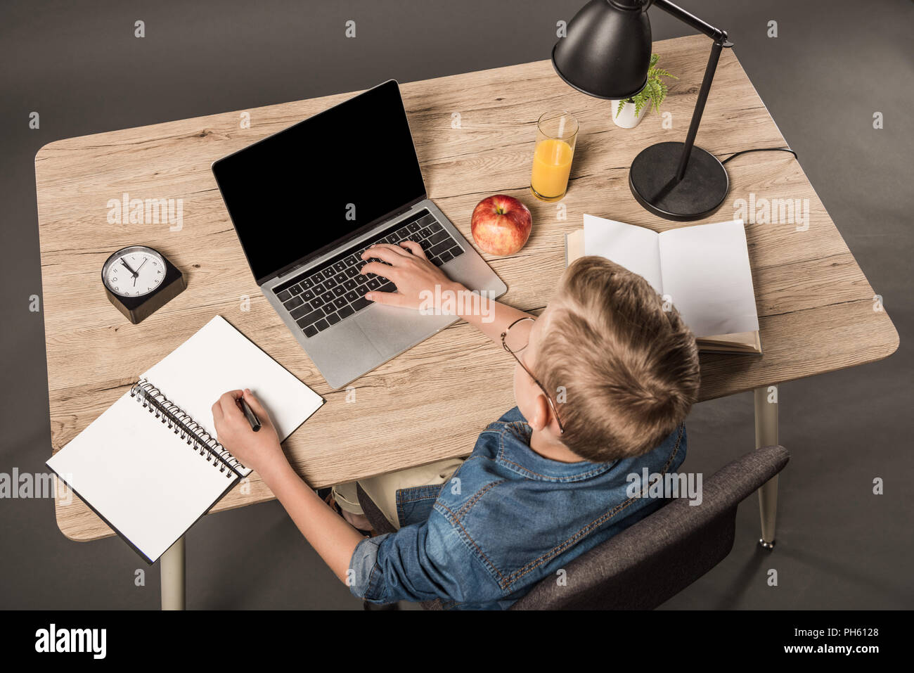 elevated view of schoolboy doing homework on laptop at table with ...