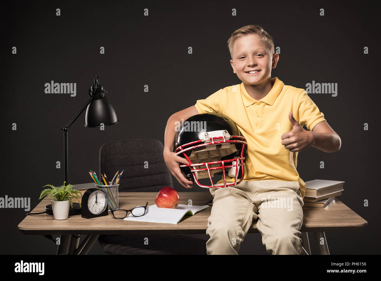 schoolboy holding american football helmet, doing thumb up gesture and