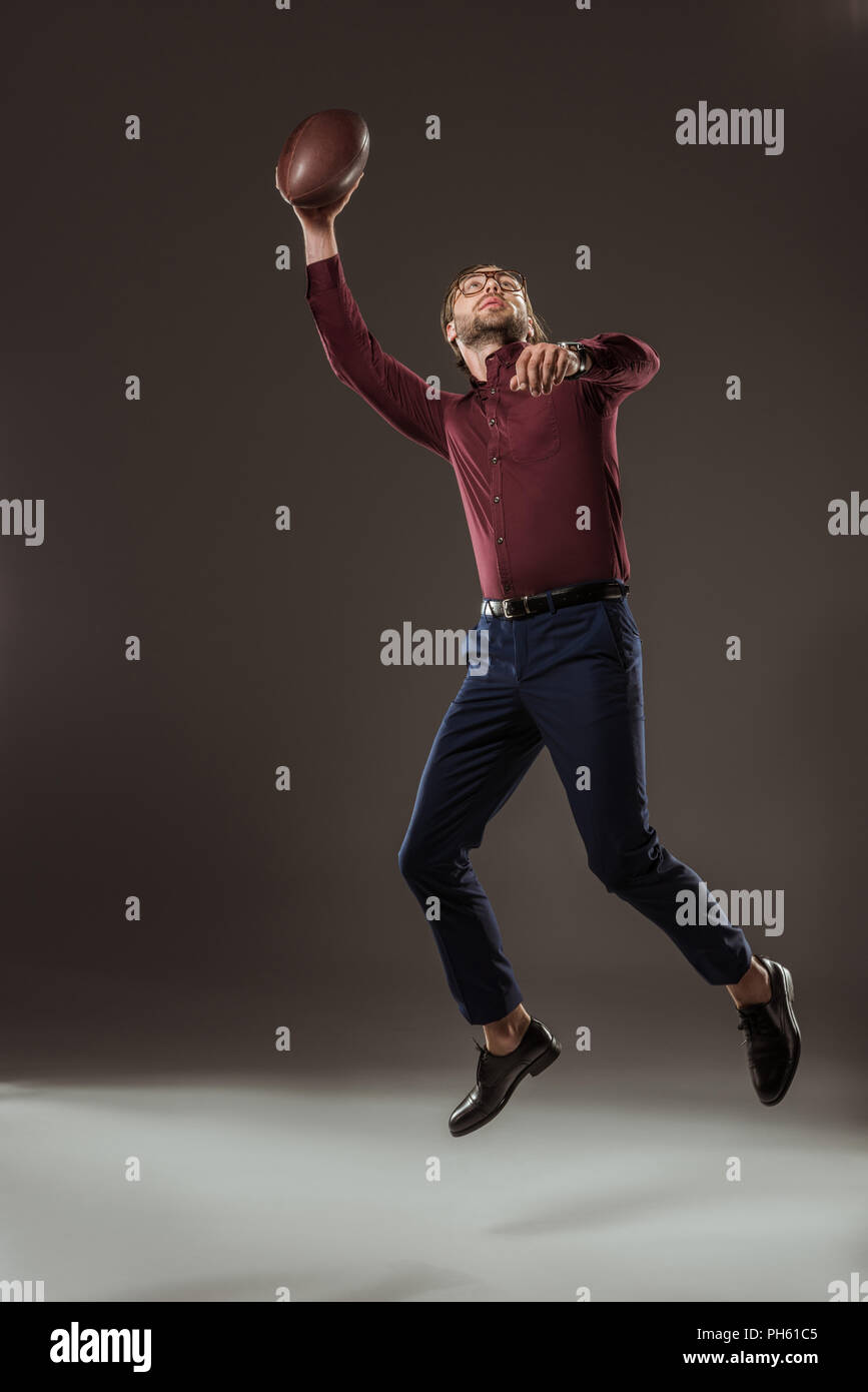 full length view of man jumping and catching rugby ball on black Stock Photo